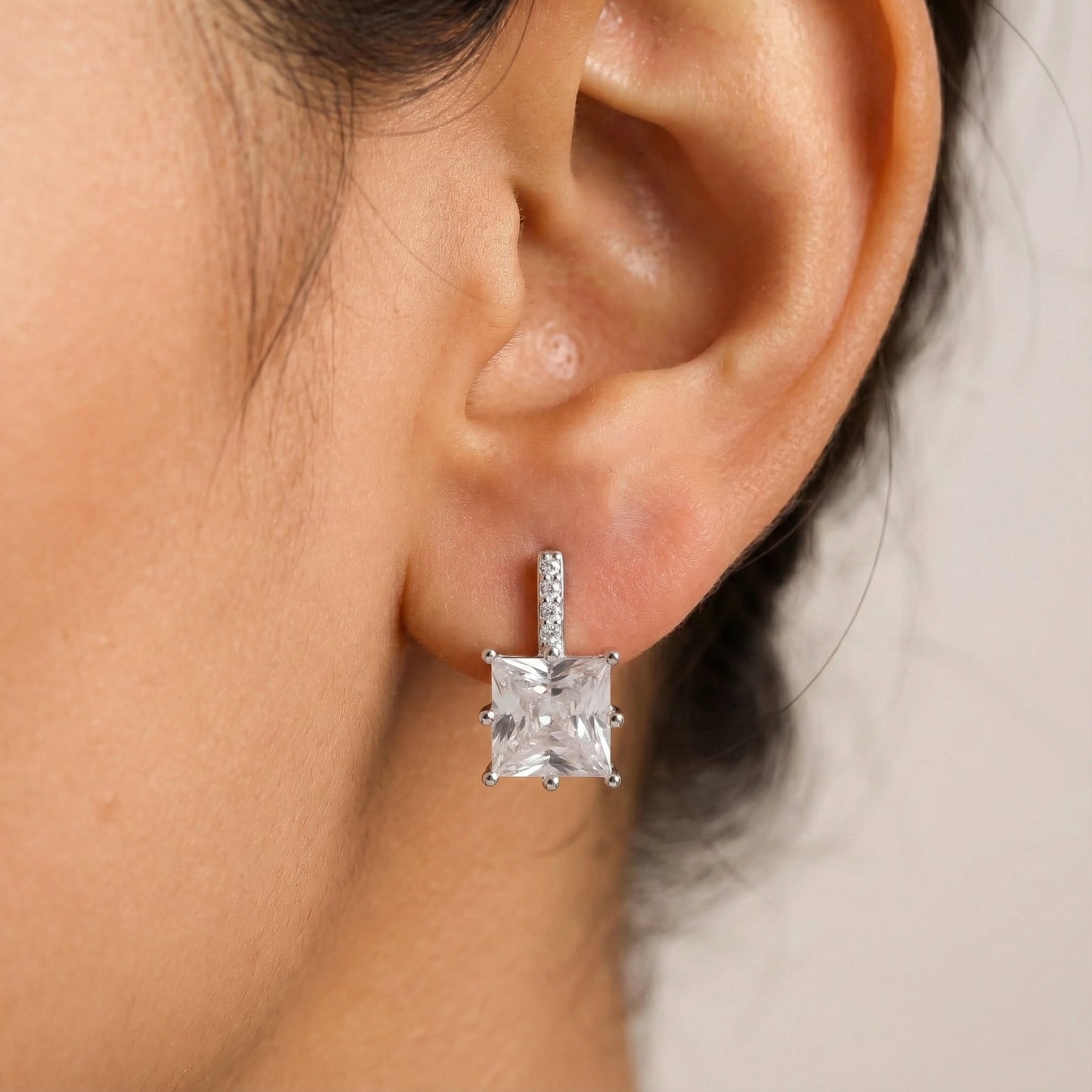Close-up of an ear wearing a diamond earring with a neutral background