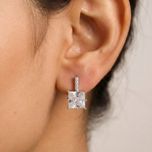 Close-up of an ear wearing a diamond earring with a neutral background