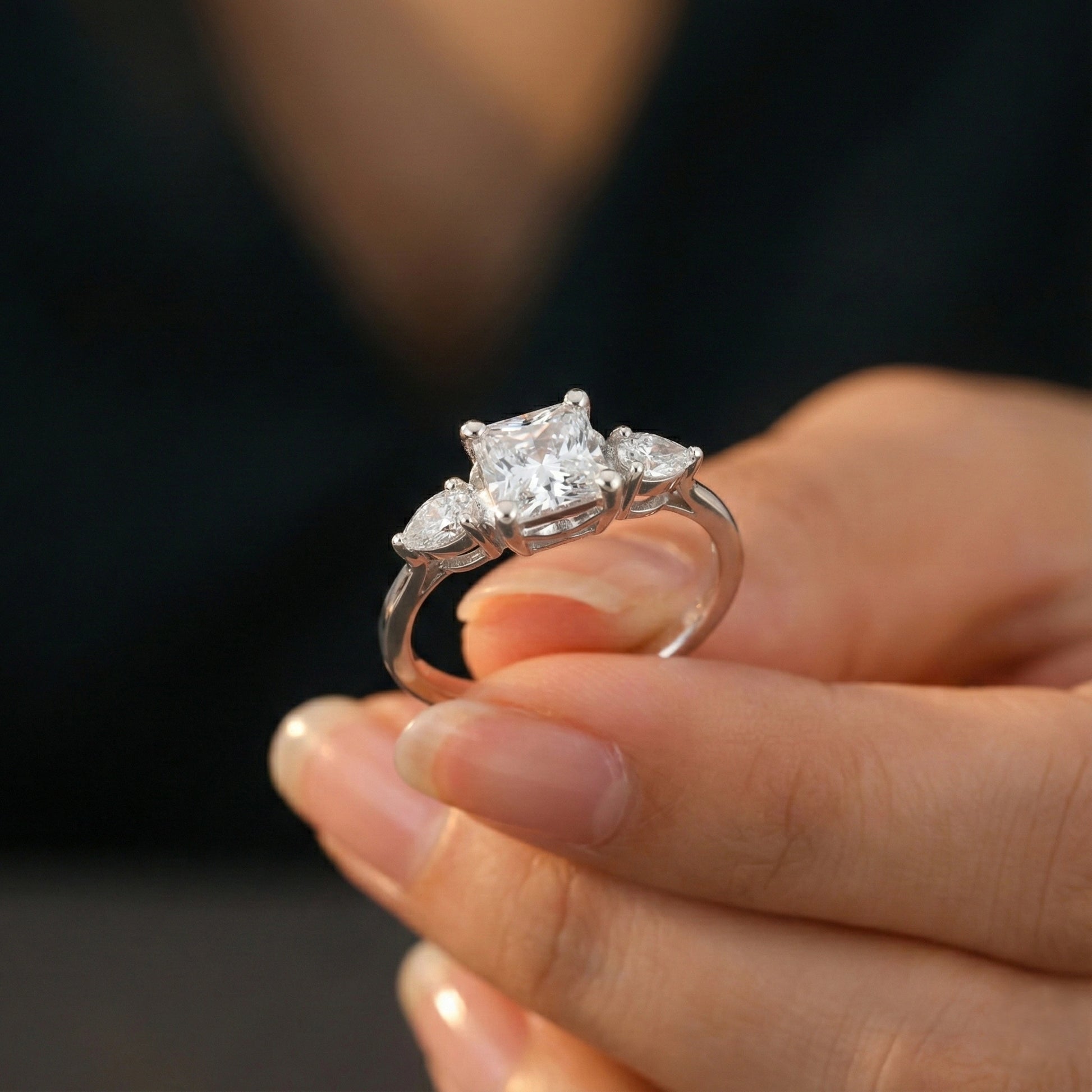 Silver ring with three diamonds held in a hand against a dark background