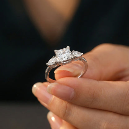 Silver ring with three diamonds held in a hand against a dark background