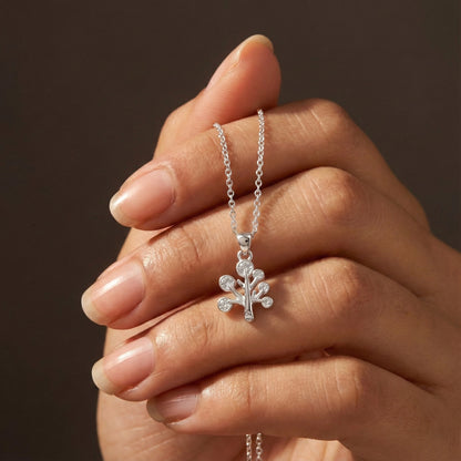 Silver necklace with a floral pendant held by a hand against a dark background