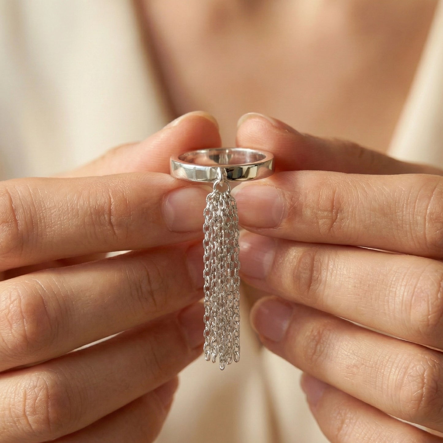 Silver ring with tassel detail held between fingers against a neutral background