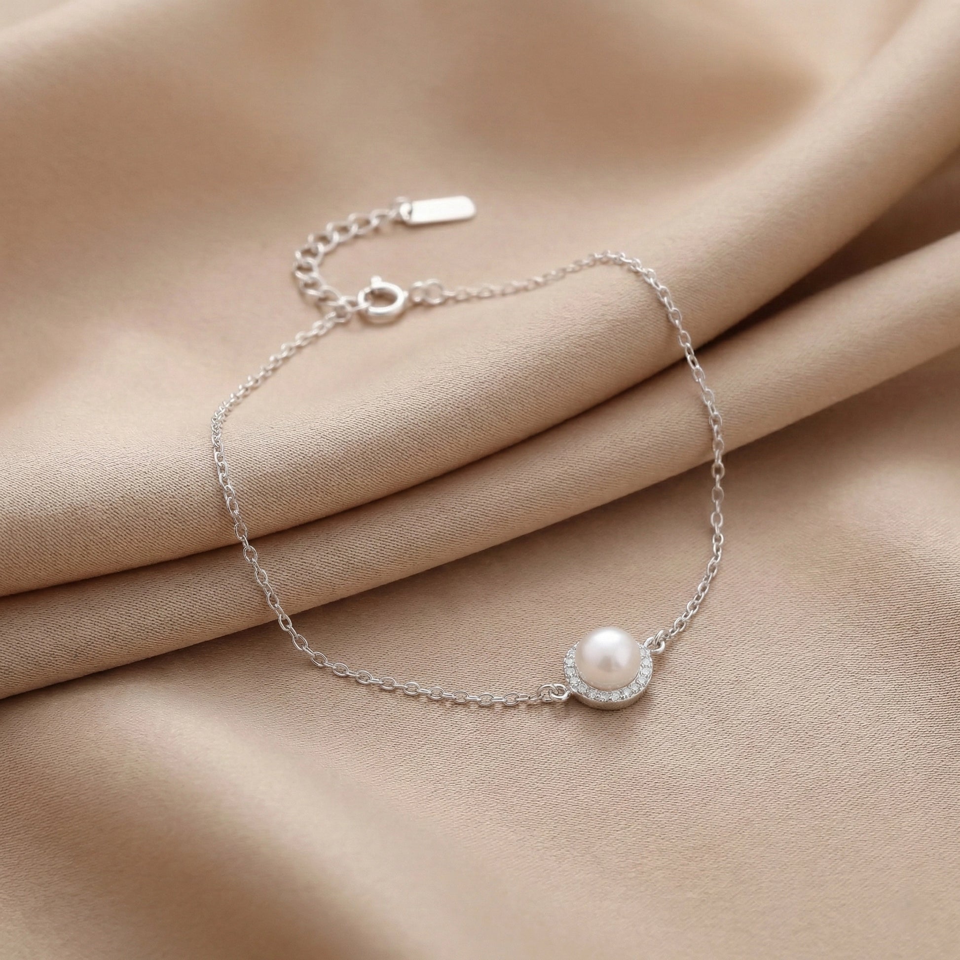 925 silver pearl charm bracelet on beige fabric background