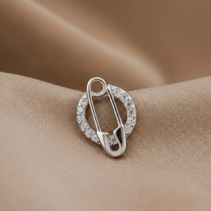 Silver safety pin-shaped brooch with clear stones on a beige fabric background
