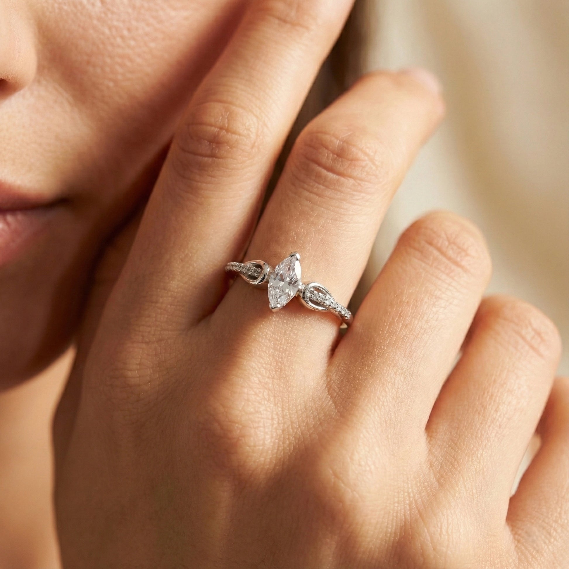 Close-up of a hand wearing a silver ring with a heart-shaped diamond on a neutral background