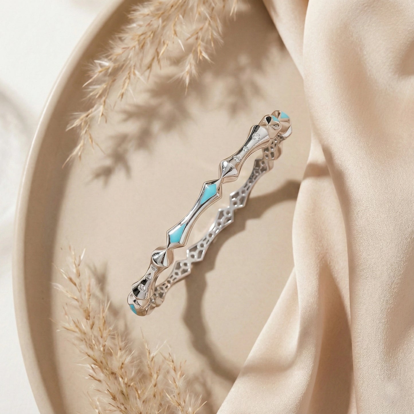 Silver bracelet with blue accents on a beige plate with fabric and dried grasses