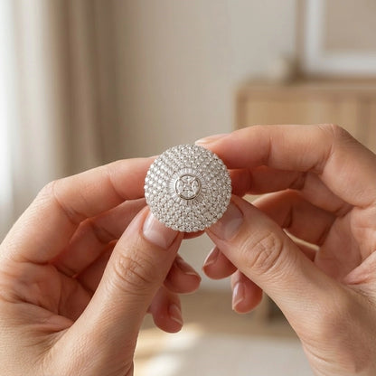 Silver jewelry box with intricate design held by hands against a neutral background