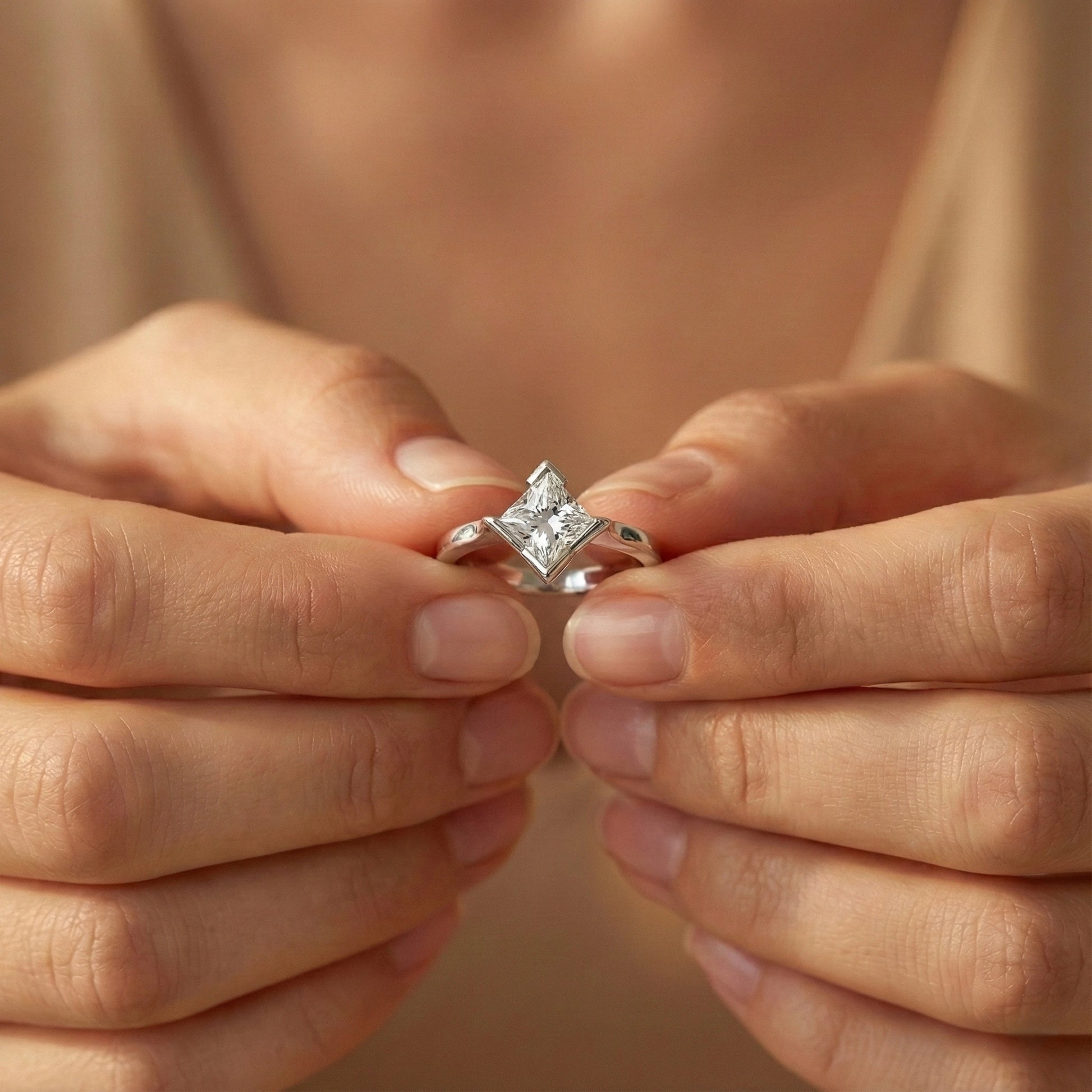 Close-up of hands holding a diamond ring against a neutral background