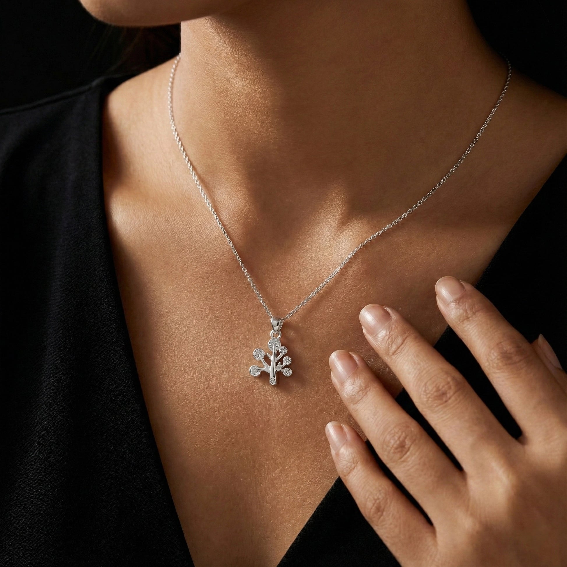 Silver necklace with a tree pendant worn by a person against a black background