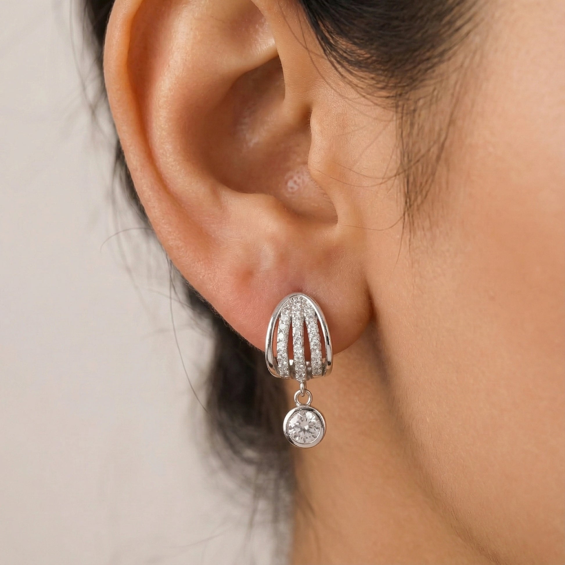 Close-up of a silver earring with a dangling gemstone on an ear against a neutral background