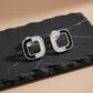 Pair of silver earrings with black accents on a dark stone surface