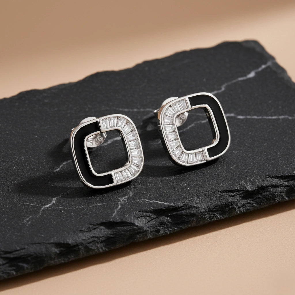 Pair of silver earrings with black accents on a dark stone surface