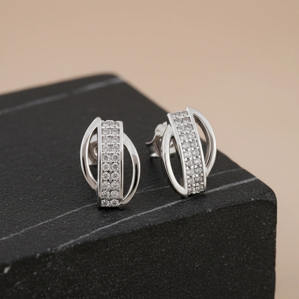 Silver earrings with diamond accents on a black stand against a beige background