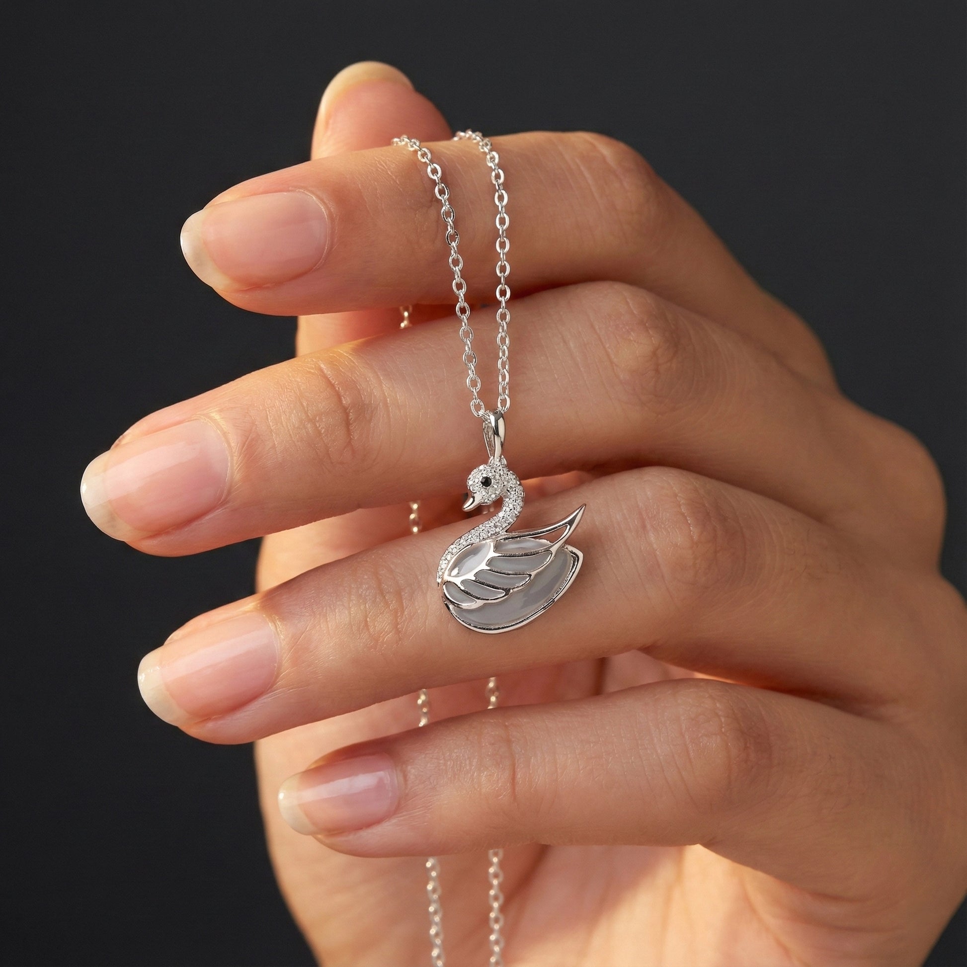 Hand holding a silver swan necklace against a dark background