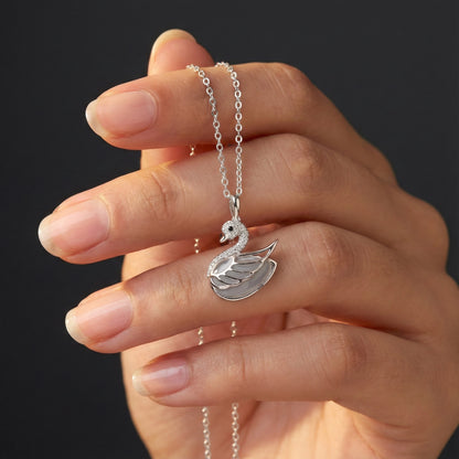 Hand holding a silver swan necklace against a dark background