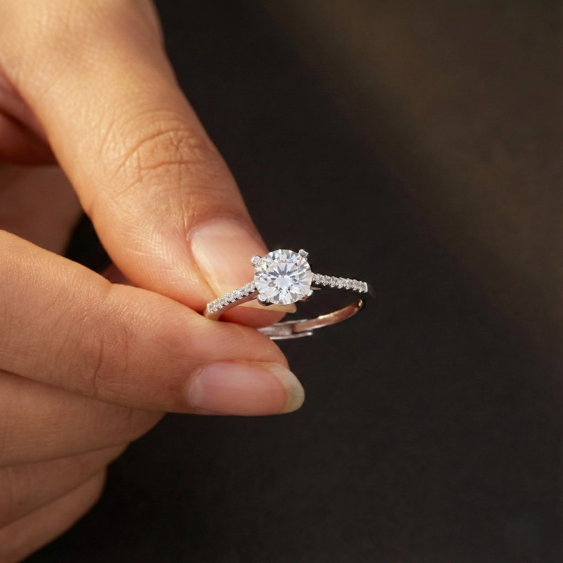 Close-up of a hand holding a diamond ring against a dark background